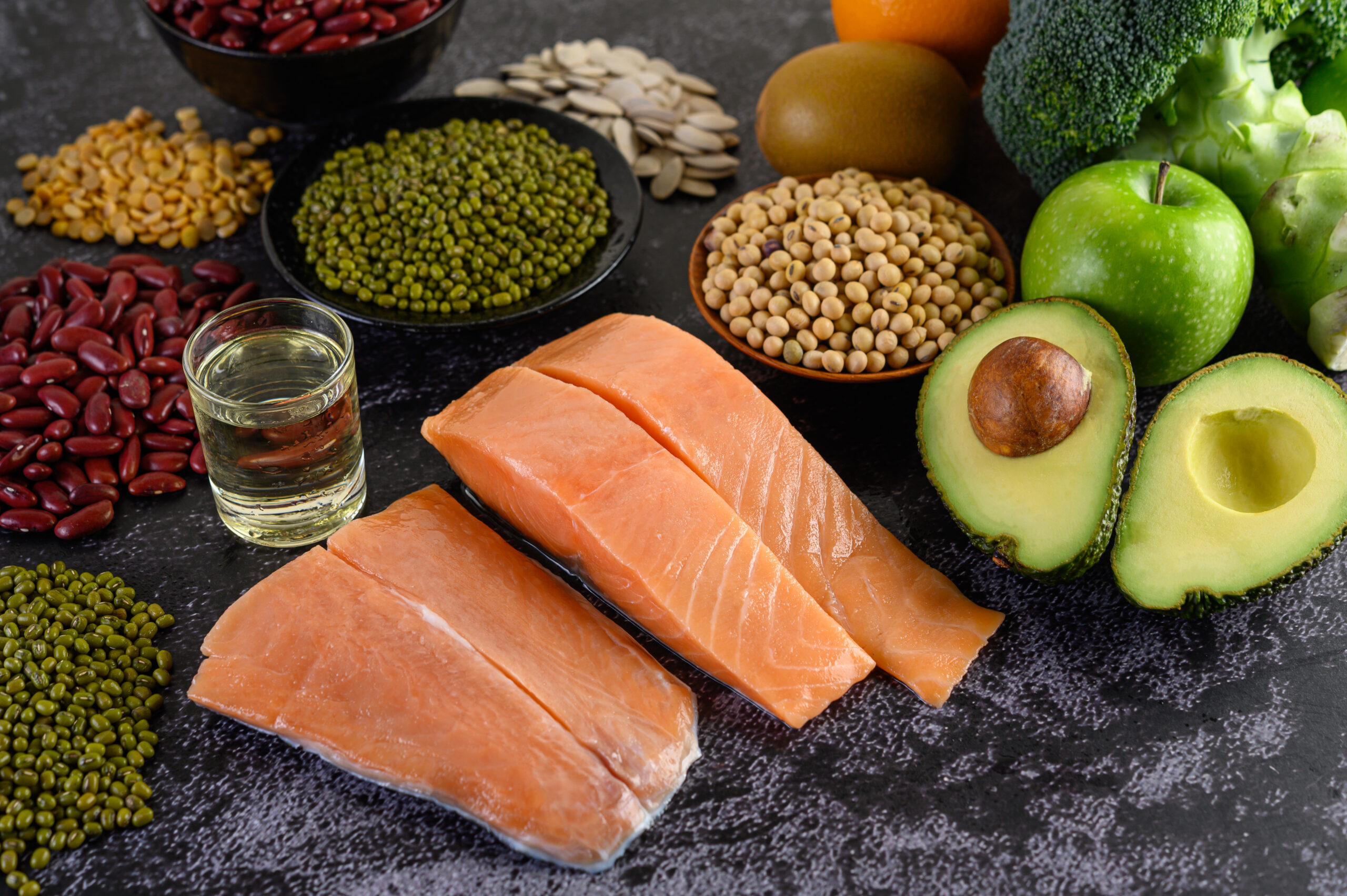Legumes, broccoli, fruit, and salmon placed on a black cement fl