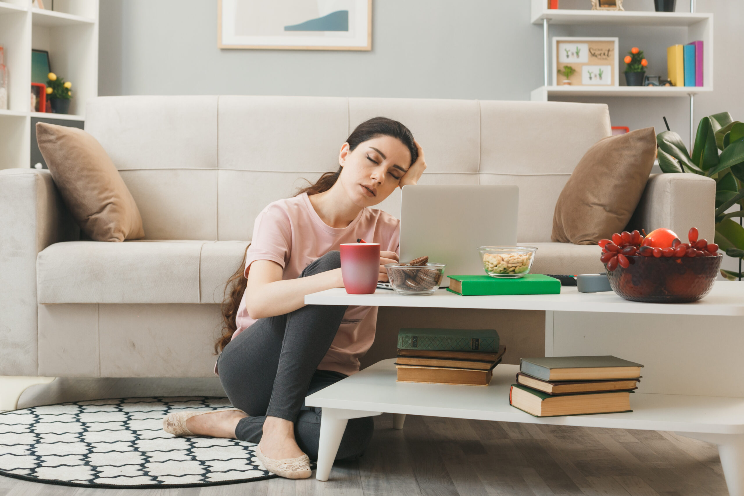 tired-with-closed-eyes-putting-hand-head-young-girl-sitting-floor-coffee-table-living-room